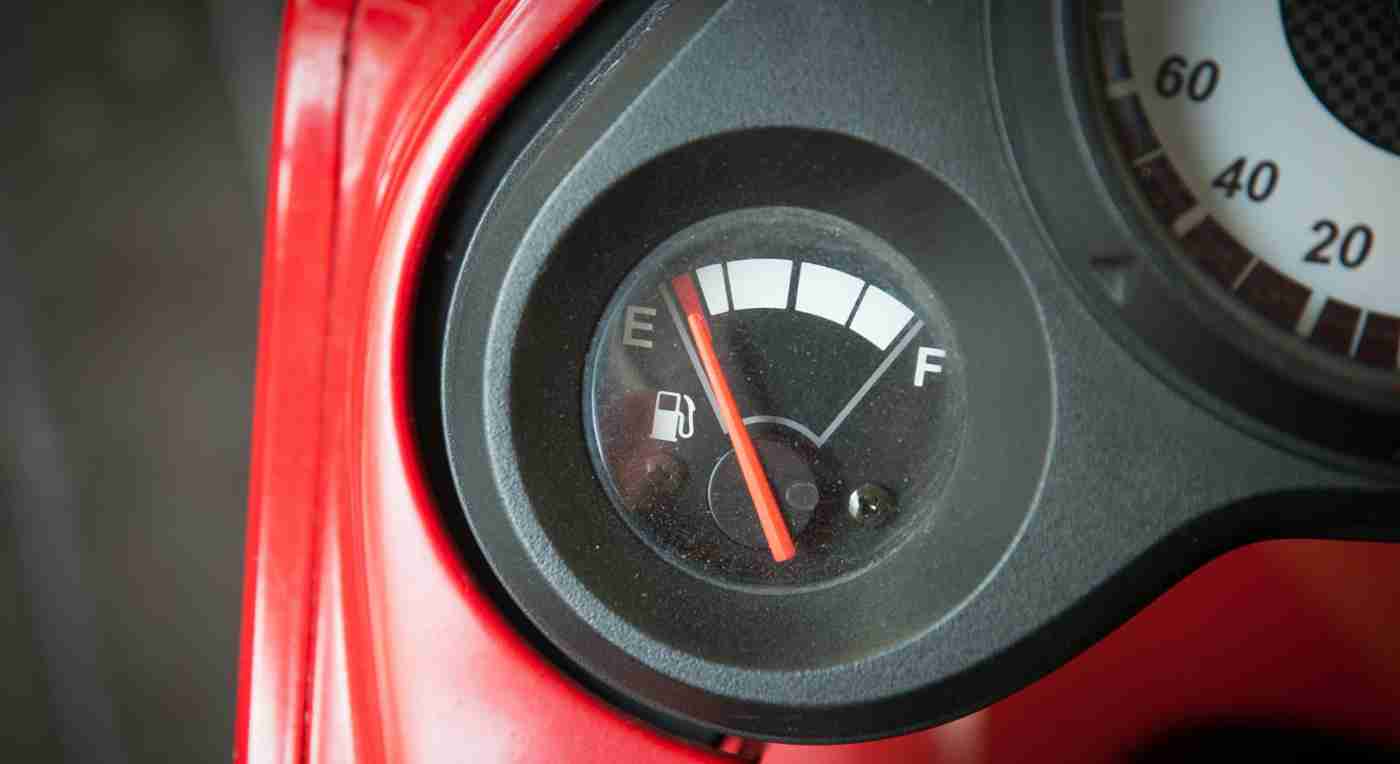 Close-up of a car fuel gauge with the needle pointing to empty, set against a red background. The image conveys urgency and a need for refueling.