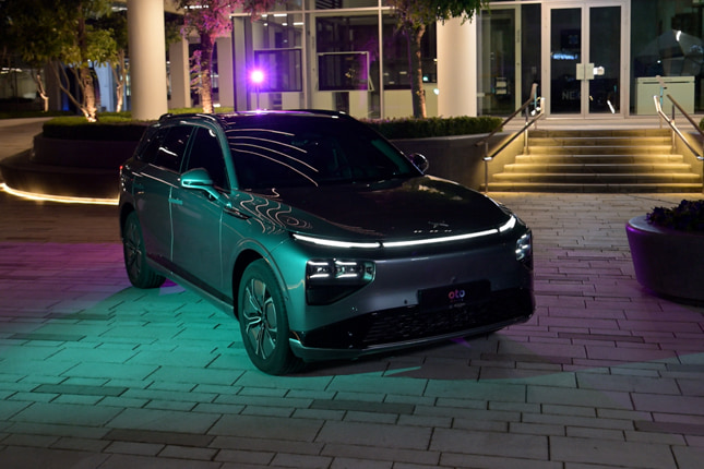Modern grey Li Auto luxury electric SUV showcased outdoors on a brick pavement under vibrant neon lighting.