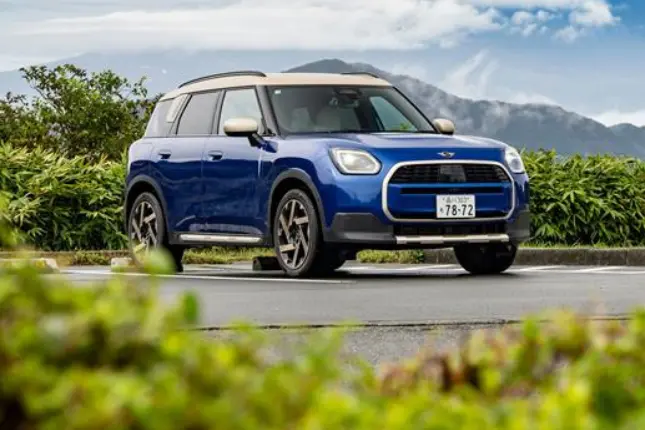 Front angle view of a blue Mini Countryman Cooper SUV parked in a scenic lot with mountains in the background.
