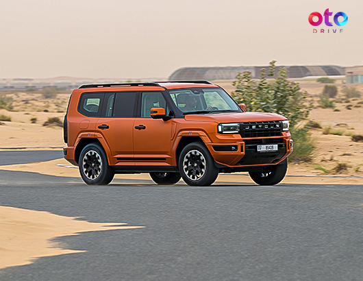Matte orange Jetour G700 luxury SUV driving fast on a paved desert highway road.