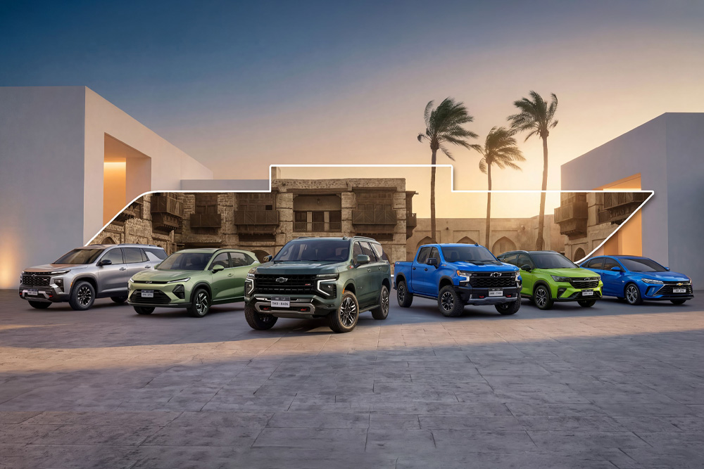 A lineup of six colorful SUVs and sedans is parked against a backdrop of modern and historical architecture at sunset, with palm trees and a light outline above them.