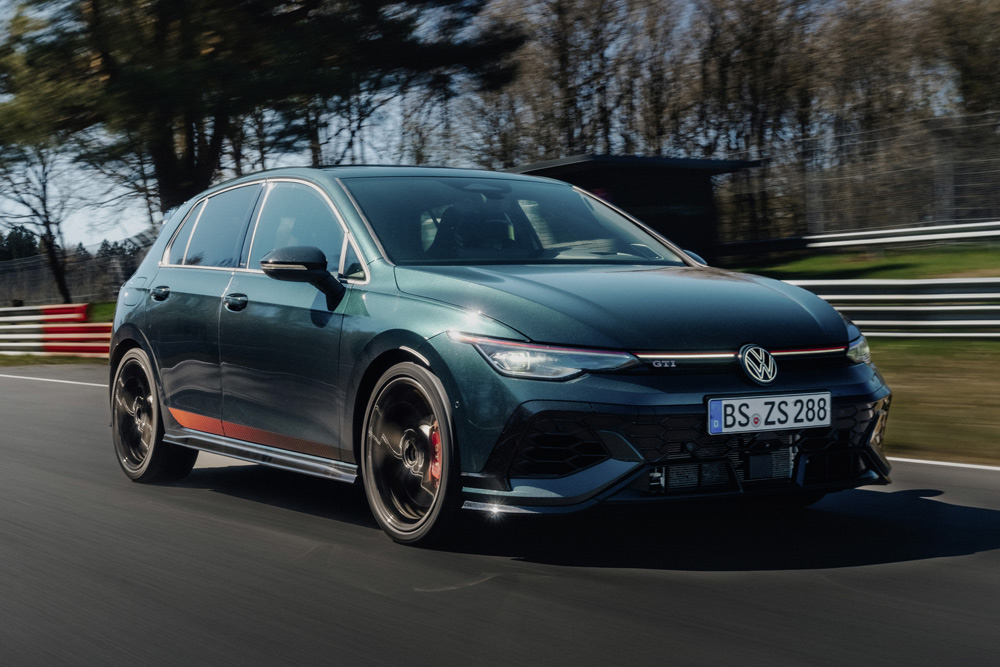 A sleek, dark green Volkswagen GTI drives energetically on a winding racetrack, with blurred trees and barriers in the background, conveying speed and agility.