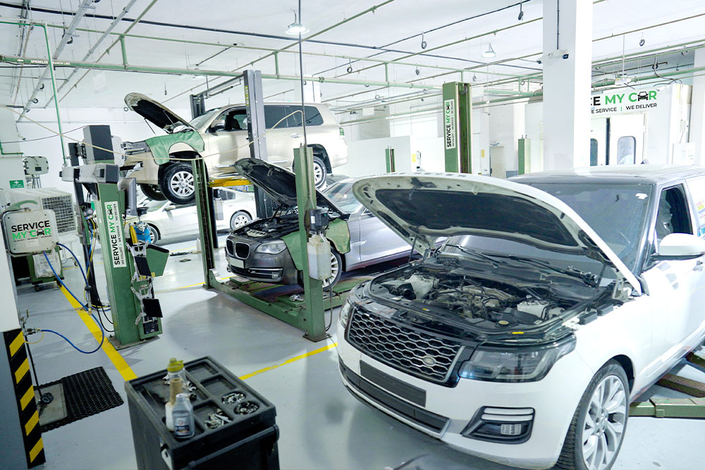 A busy car repair shop with lifted vehicles having open hoods for maintenance on hydraulic lifts. Bright lighting gives a clean and professional atmosphere.