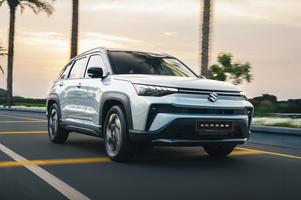 A sleek, white Suzuki SUV drives on a palm tree-lined road at sunset. The car's modern design and shiny exterior convey a sense of luxury and freedom.