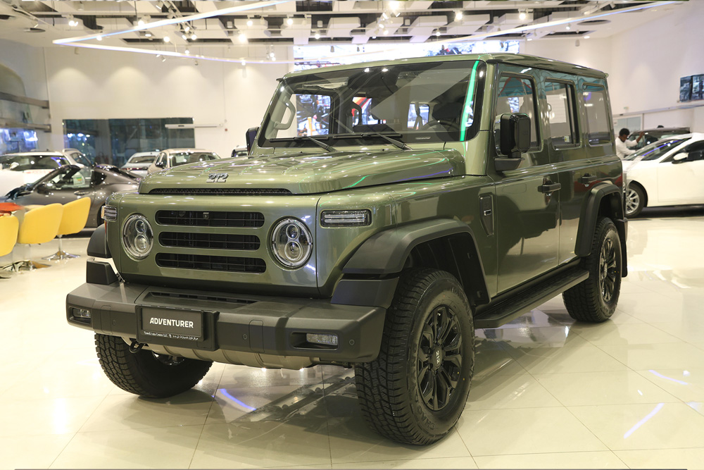 An olive green BAW 212 Adventurer 4x4 rugged off-road SUV showcased inside a brightly lit modern automotive showroom.
