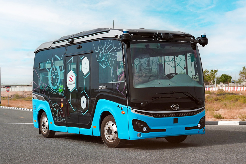 Futuristic cyan and black King Long autonomous smart minibus parked on an asphalt roadside under a clear sky.