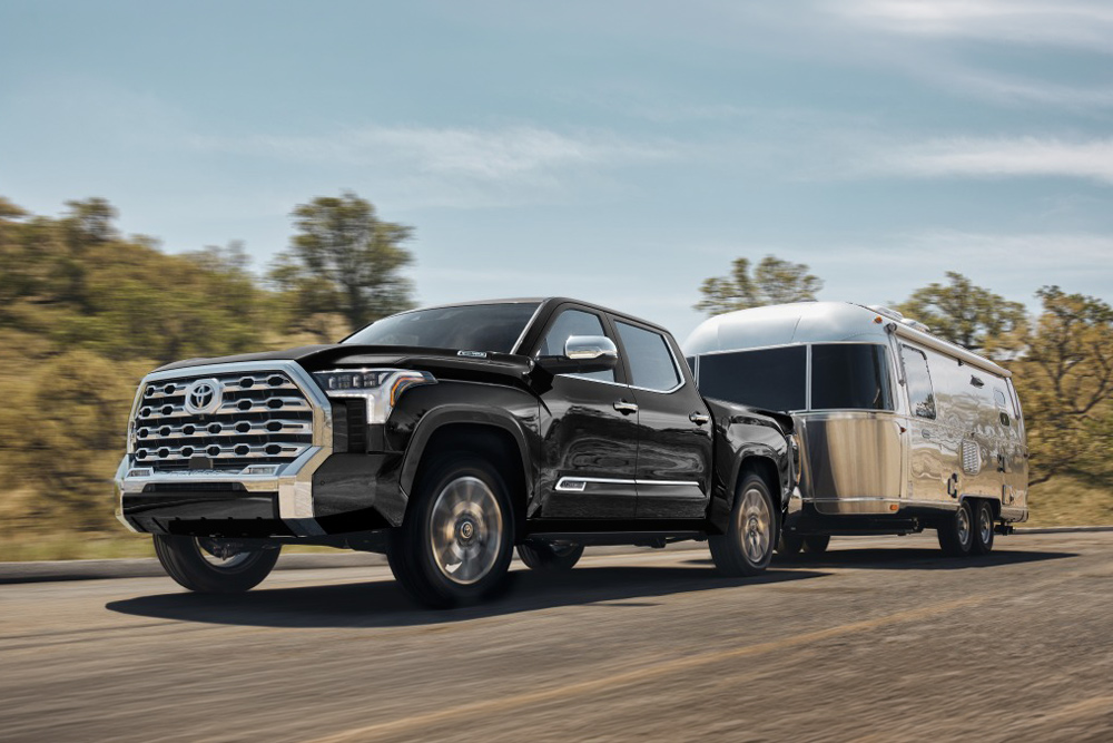 Black Toyota Tundra pickup truck driving on an asphalt highway road while towing a silver Airstream trailer.