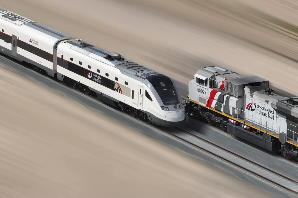 High-angle view of a sleek white Etihad Rail high-speed passenger train moving along desert tracks.