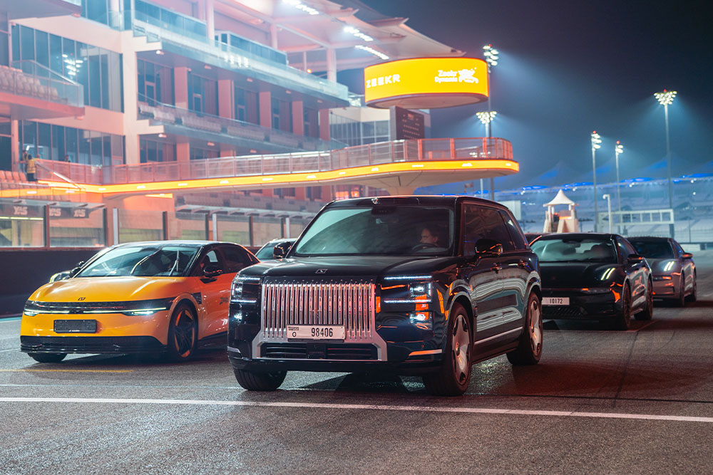 A dark luxury Zeekr 009 SUV lined up next to a bright yellow electric sedan on a race track at night.