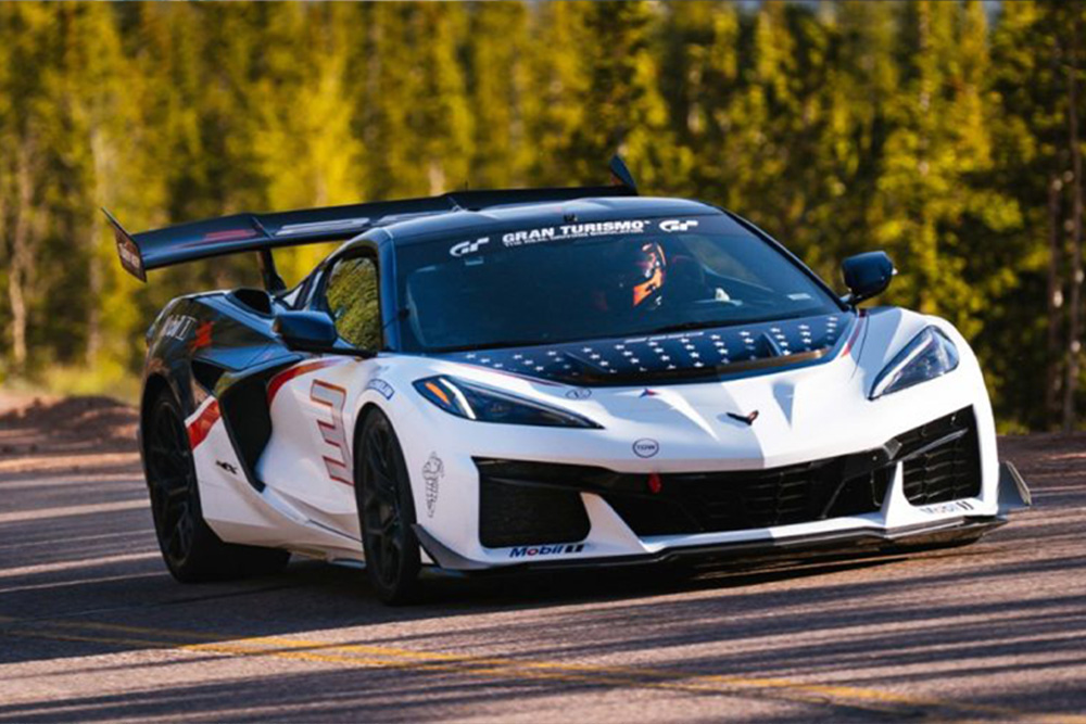 White Chevrolet Corvette racing sports car with stars and stripes graphic decals driving fast on a race track loop.