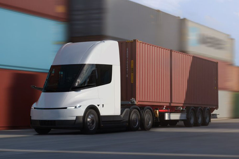 Dynamic front three-quarter view of a white autonomous electric semi-truck hauling a shipping container
